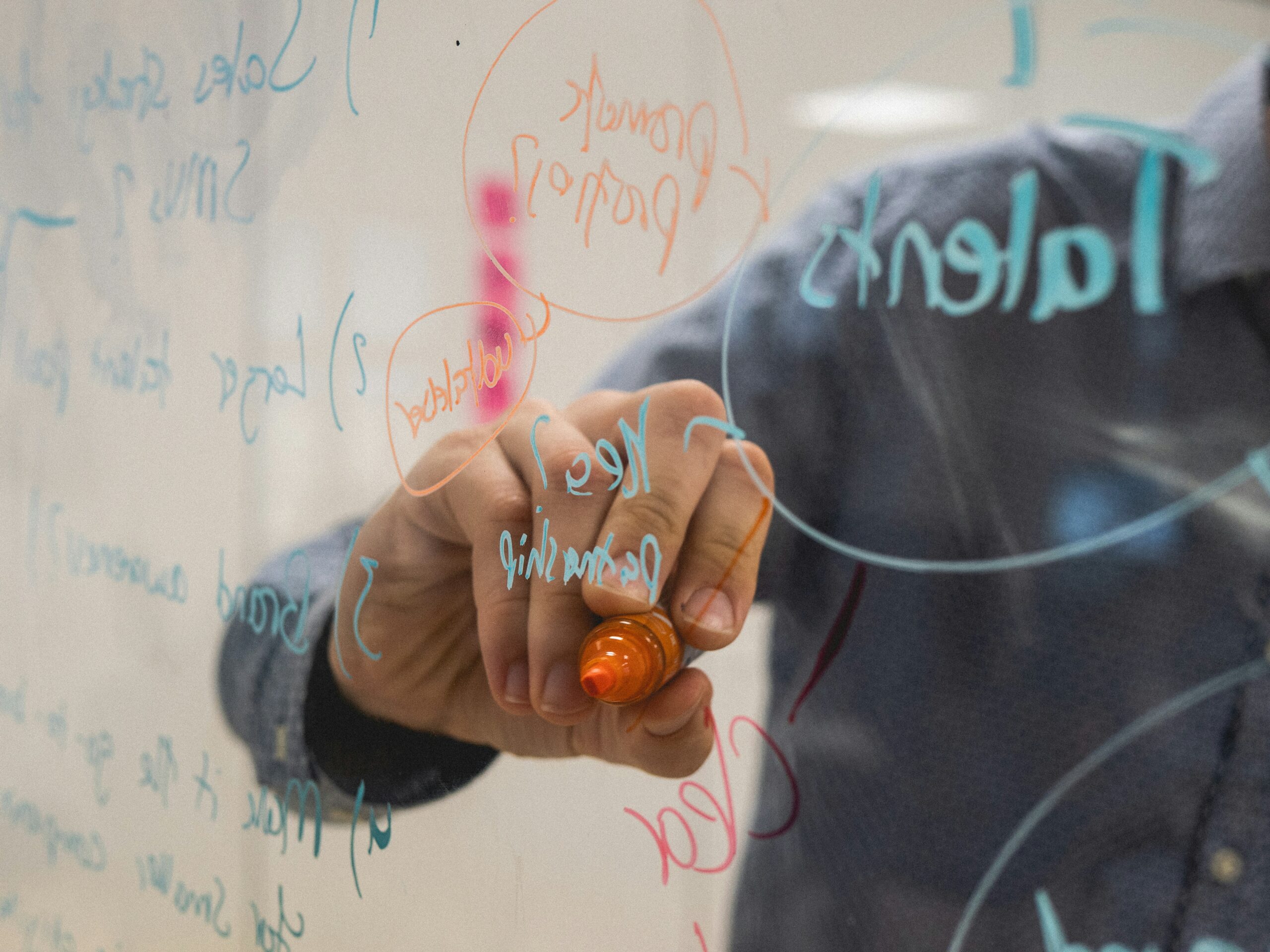How Creative Business Videos Help B2B Brands Stand Out 2 A close-up of someone's hand writing words and numbers on a clear board, representing the planning of creative business videos.